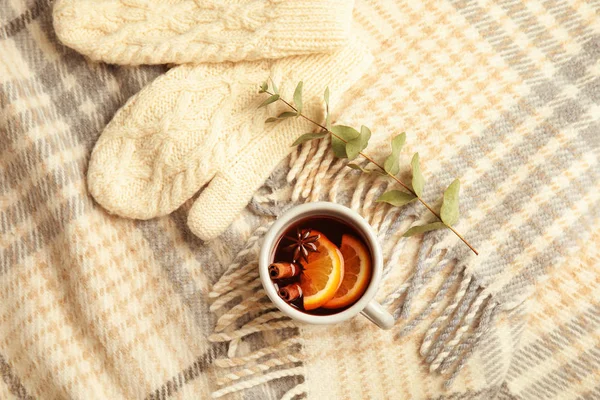 Composition with cup of hot winter drink and knitted mittens on warm plaid. Cozy season