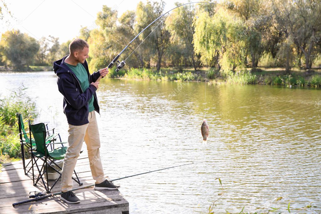 Man with rod fishing on wooden pier at riverside. Recreational activity