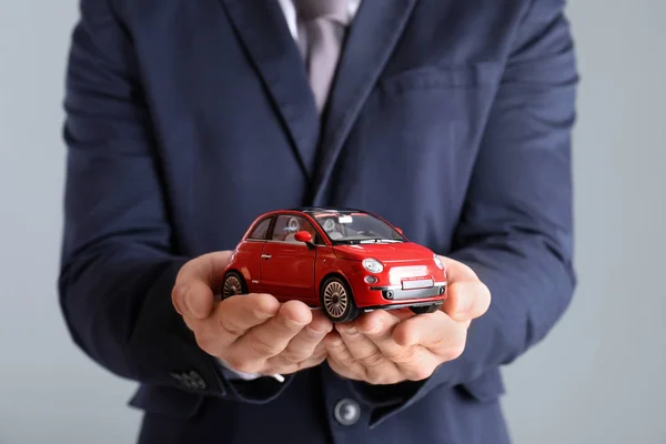 Männlicher Versicherungsvertreter Hält Spielzeugauto Auf Grauem Hintergrund Nahaufnahme — Stockfoto
