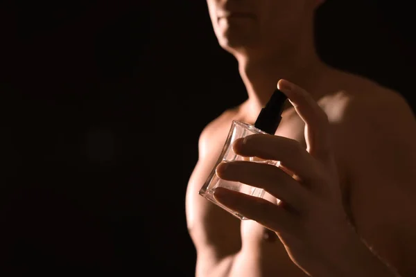 Young man with perfume bottle on black background, closeup. Space for text