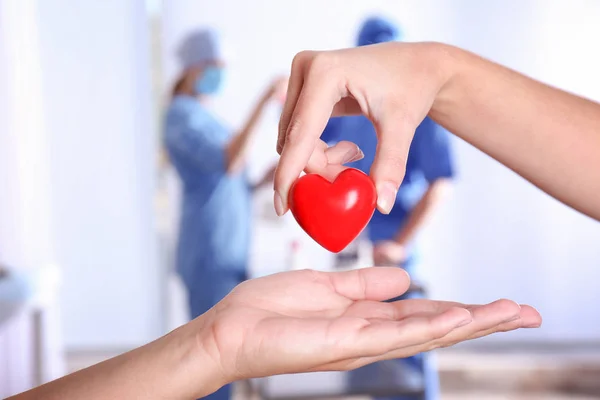 Doctor giving red heart to patient, closeup. Donation day