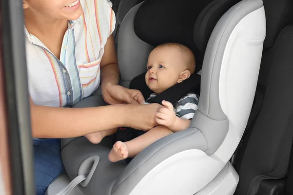 Mother fastening baby to child safety seat inside of car