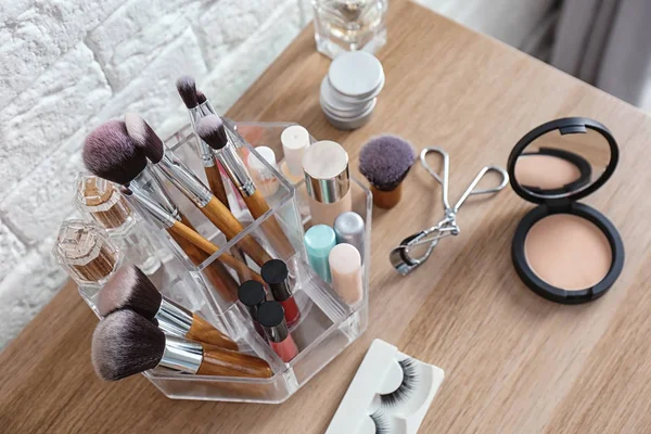 Organizer with cosmetic products for makeup on table near brick wall