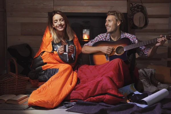年轻的旅行者在睡袋弹吉他为他的女朋友在室内 — 图库照片