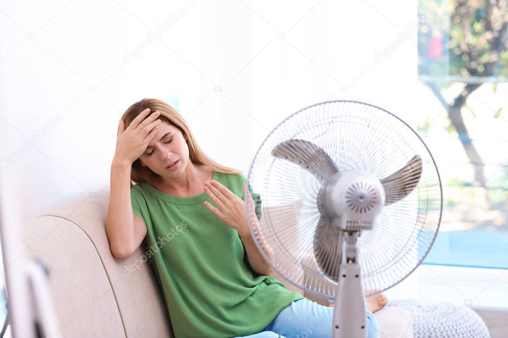 Woman suffering from heat in front of fan at home