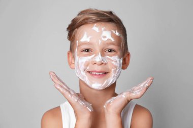 Sevimli küçük çocuk gri arka plan karşı yüz sabun köpüğü ile
