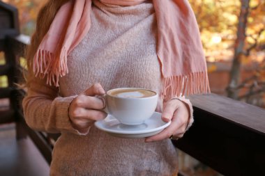 Kadın sıcak kazaklı fincan sıcak sıcak içecek ile balkonda holding