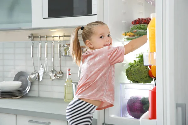 Cute girl choosing food from refrigerator in kitchen