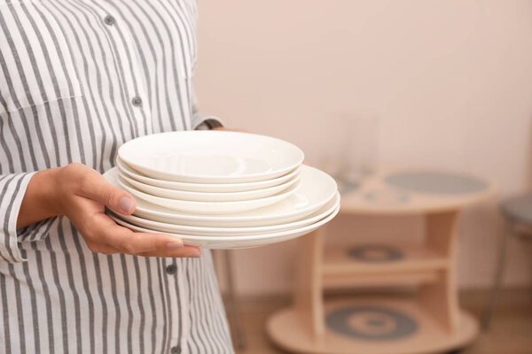 Woman holding stack of clean dishes in kitchen, closeup. Space for text