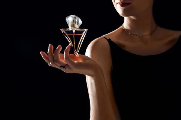Young woman with perfume bottle on black background, closeup