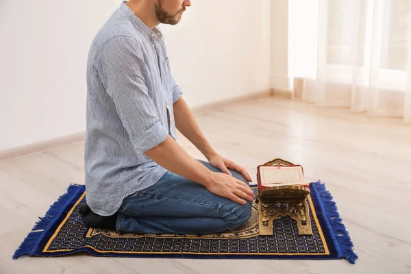 Muslim man with Koran praying on rug indoors, closeup