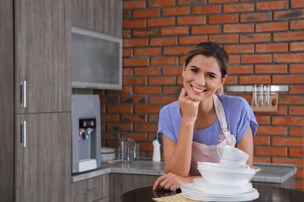 Женщина с чистой посудой за столом на кухне
