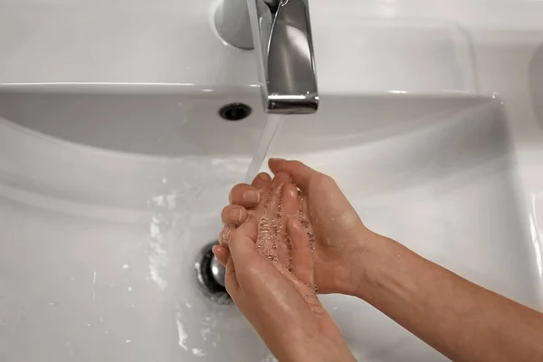 Woman washing hands under tap indoors, closeup