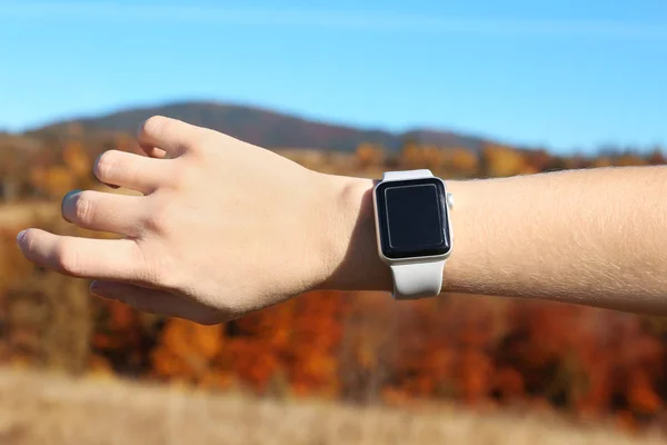 Woman checking smart watch with blank screen in wilderness, closeup