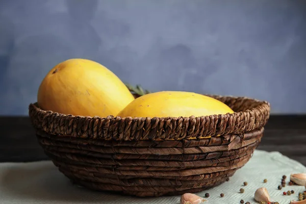 Basket with ripe spaghetti squashes on table against color background