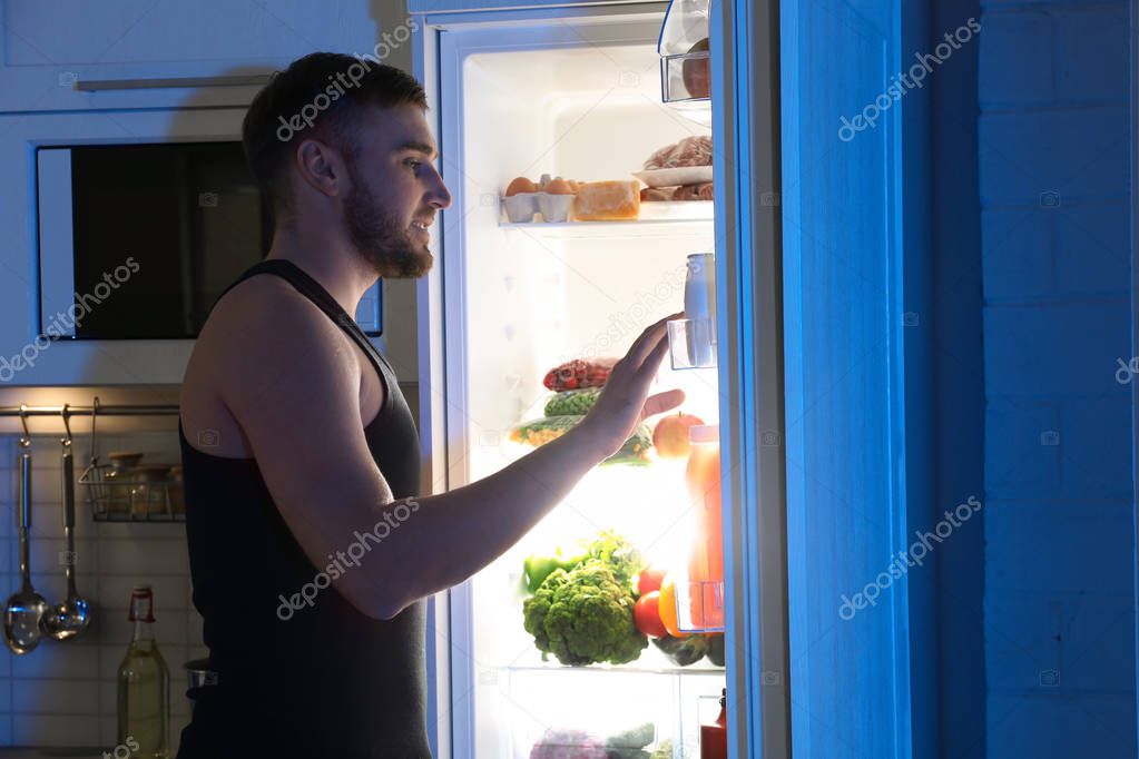 Man looking into refrigerator and choosing products in kitchen at night