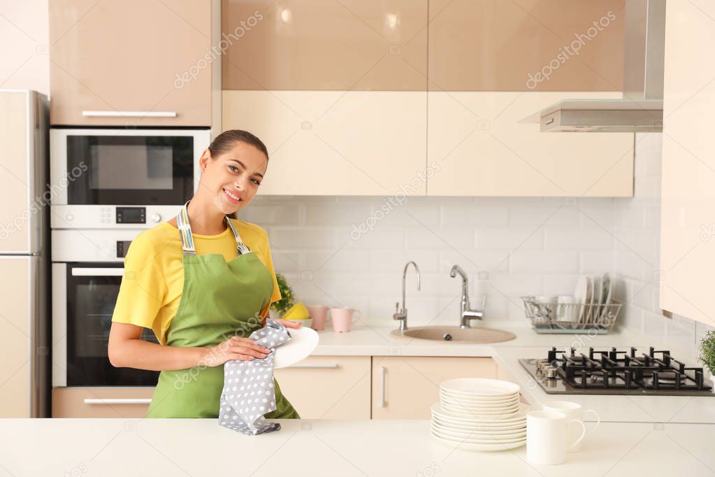 Young woman wiping clean plate in kitchen. Dish washing