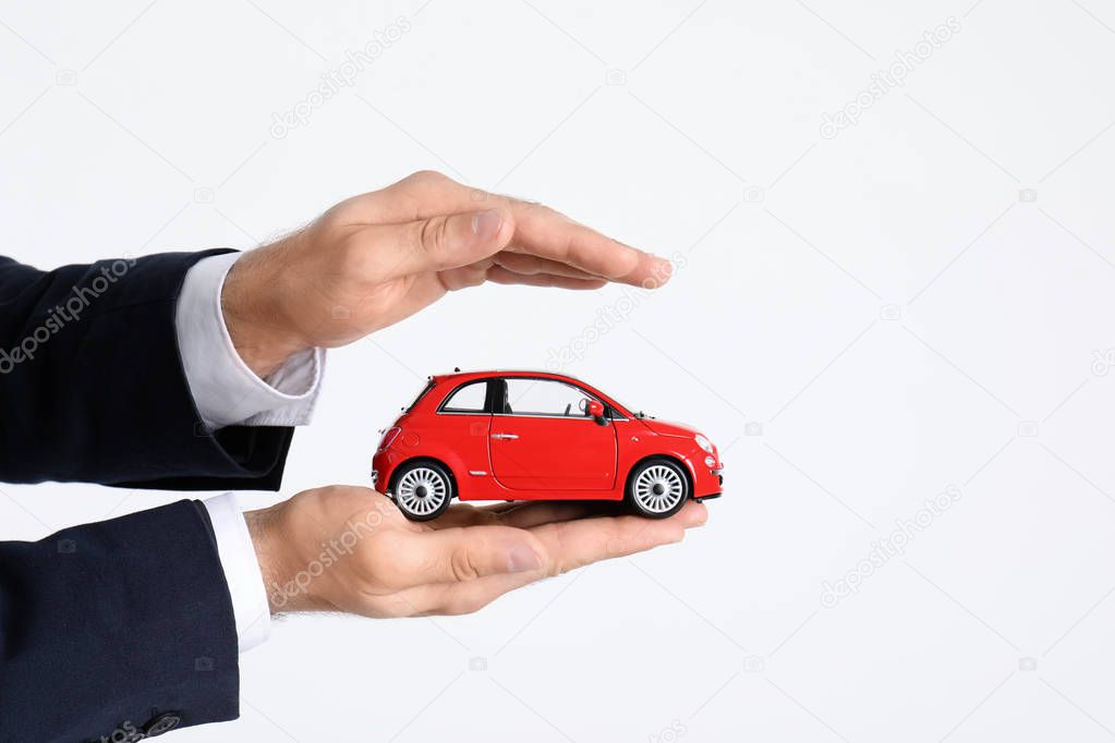 Male insurance agent holding toy car on white background, closeup. Space for text