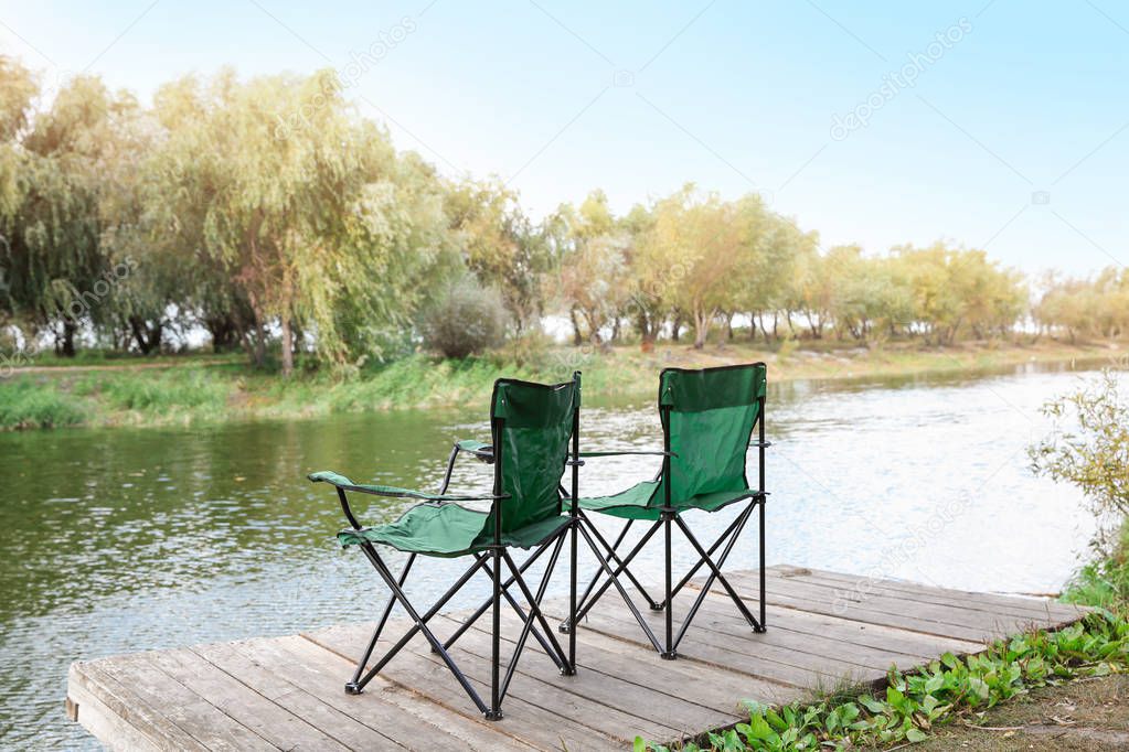 Fishing chairs on wooden pier near river