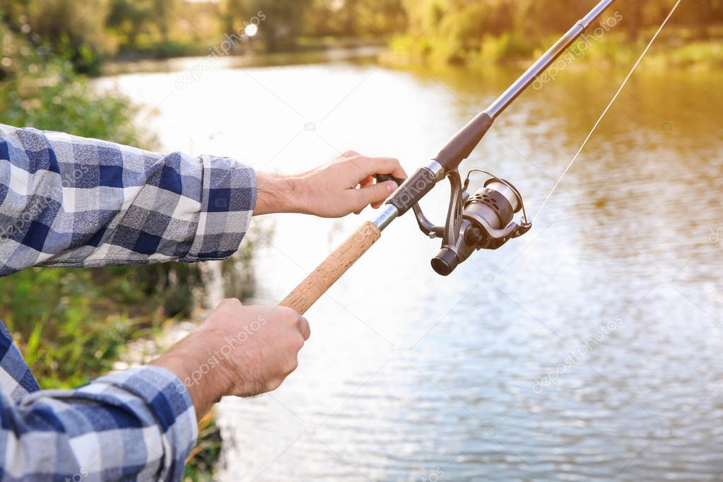 Man with rod fishing at riverside, focus on hands. Recreational activity