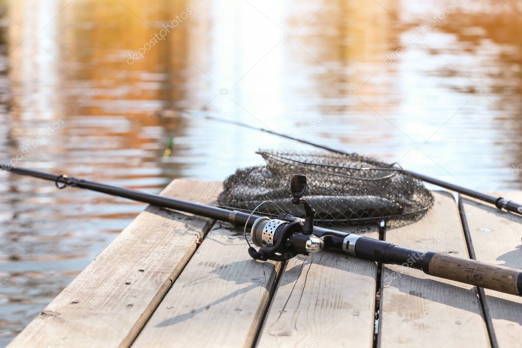 Fishing rods and fresh fish on wooden pier near pond