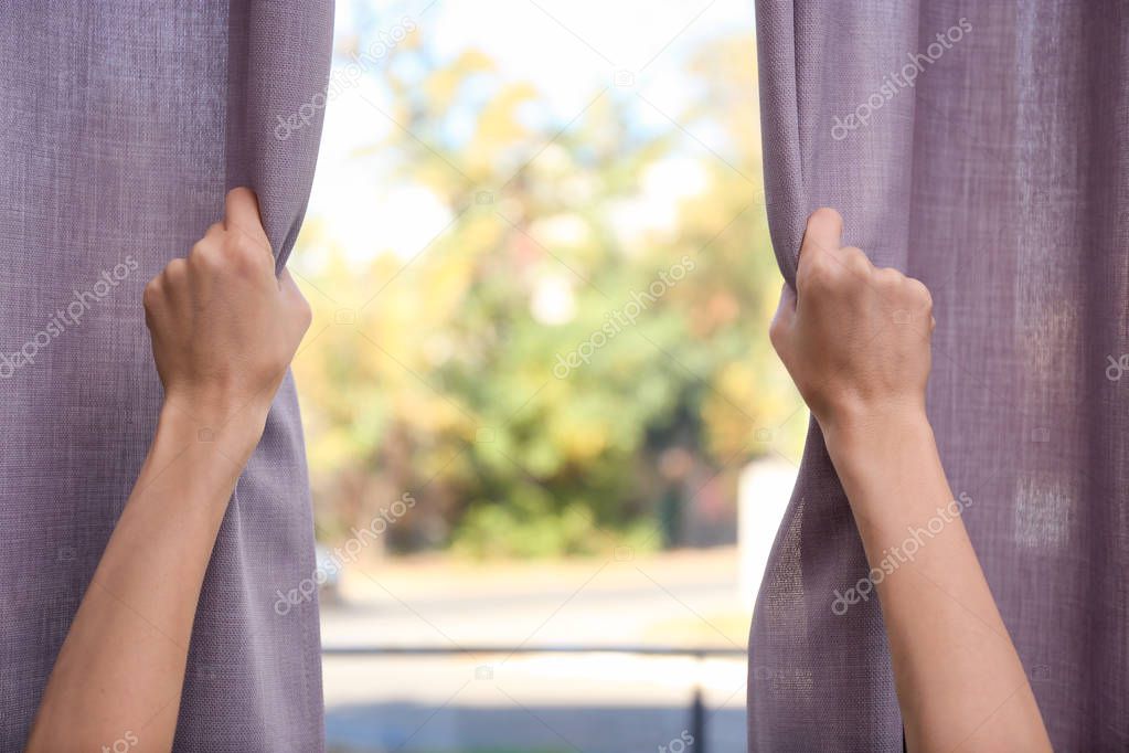 Woman opening window curtains at home, closeup. Space for text