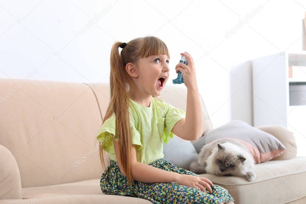 Little girl using asthma inhaler near cat at home. Health care