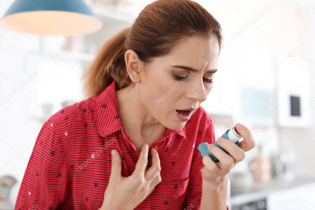 Young woman using asthma inhaler in kitchen