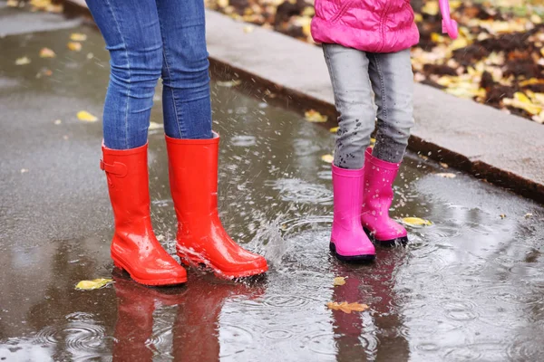 母と娘の身に着けているゴム製のブーツ足の焦点 雨の日に水たまりではね 秋の散歩 — ストック写真