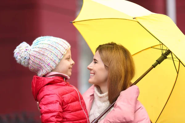 Mother and daughter with umbrella in city on autumn rainy day