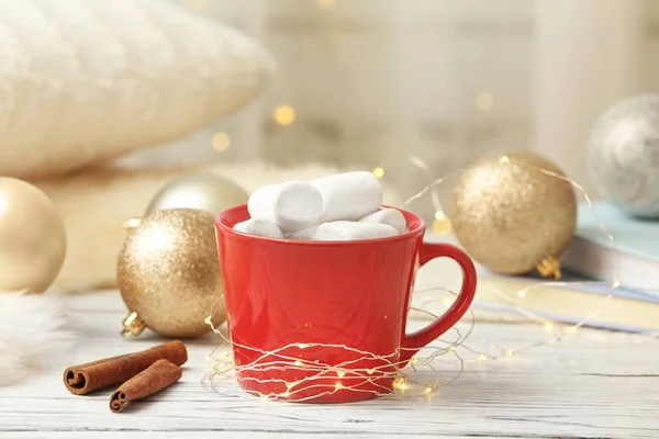 Composition with cup of hot winter drink and Christmas lights on table. Cozy season