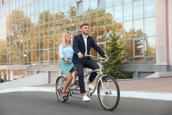 Couple riding tandem bike on city street