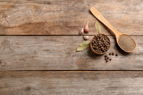 Flat lay composition with allspice peppercorns in bowl and space for text on wooden background