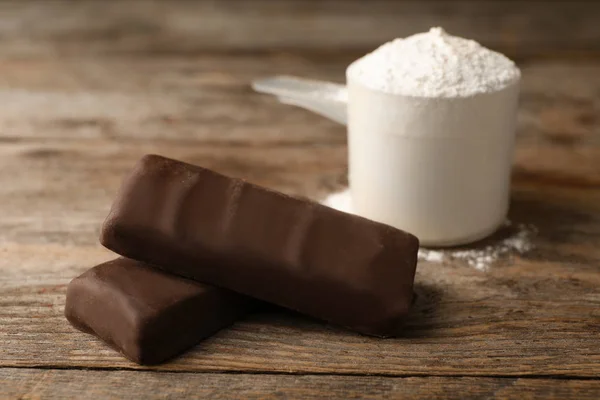 Tasty protein bars and scoop of powder on wooden table