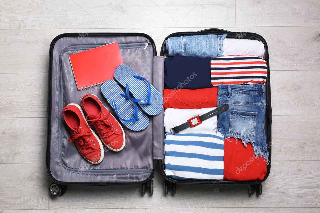 Packed suitcase with stuff on wooden background, top view