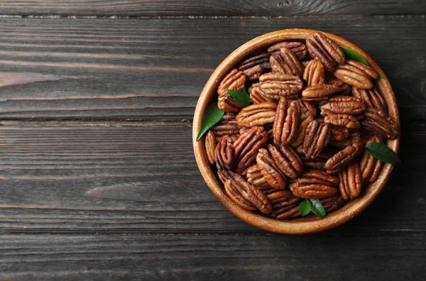 Dish with shelled pecan nuts on wooden background, top view. Space for text