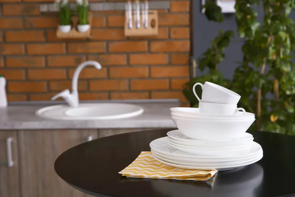 Stack of clean dishes and cups on table against blurred background. Space for text