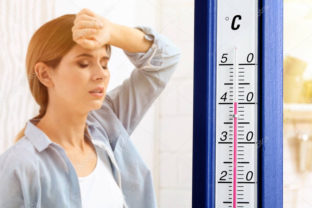 Extreme high temperature on thermometer and woman suffering from heat indoors
