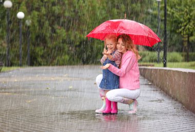 Mutlu anne ve kızı yağmurlu bir gün Park'ta kırmızı şemsiye ile. Metin için yer