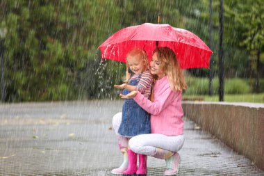 Mutlu anne ve kızı yağmurlu bir gün Park'ta kırmızı şemsiye ile. Metin için yer