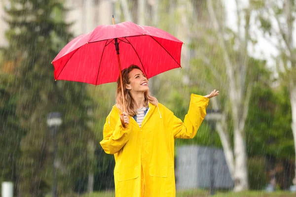 雨の日に公園で赤い傘を持つ幸せな若い女性の肖像画 — ストック写真