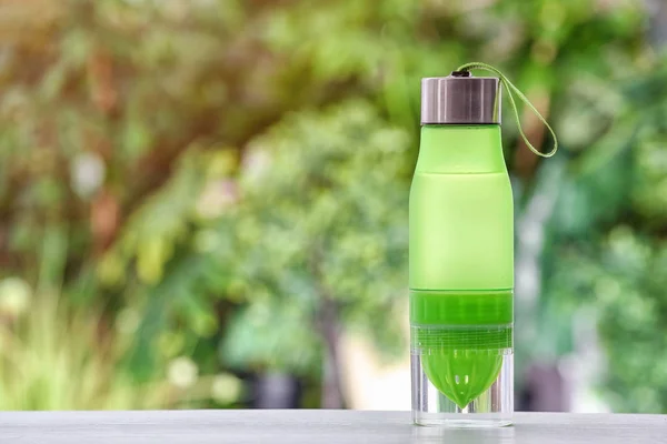 Sports water bottle on table against blurred background. Space for text