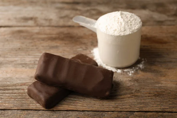 Tasty protein bars and scoop of powder on wooden table