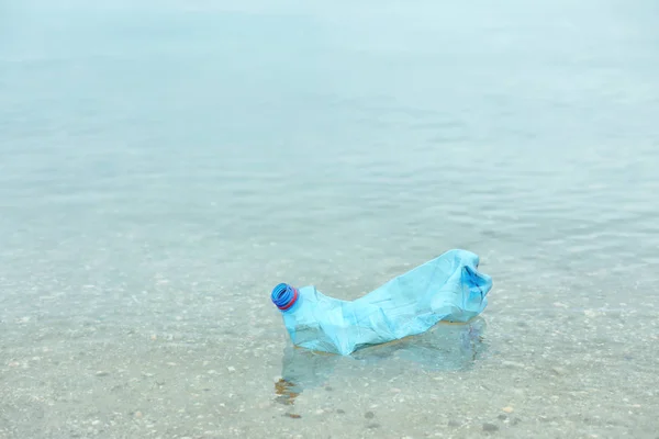 Used plastic bottle floating on water surface, space for text. Recycling problem