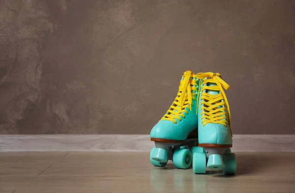 Vintage roller skates on floor near brown wall. Space for text