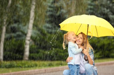 Mutlu anne ve kızı Park'ta yağmurlu bir gün sarı şemsiye ile portresi. Metin için yer
