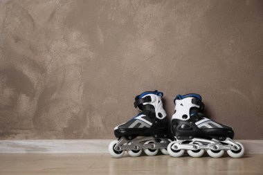 Inline roller skates on floor near brown wall. Space for text clipart