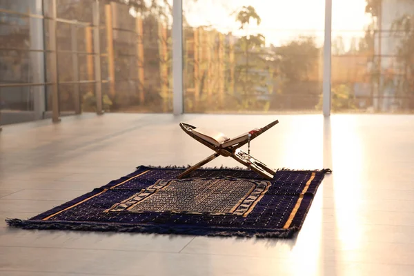 Rehal with open Quran and Muslim prayer beads on rug indoors