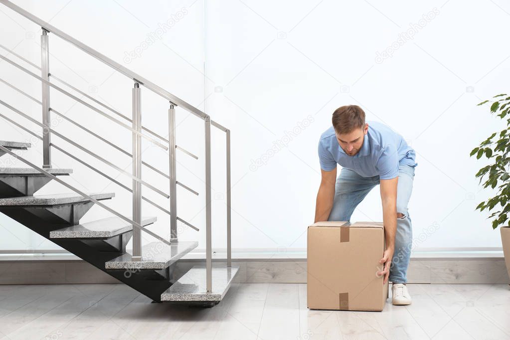 Young man lifting carton box indoors. Posture concept