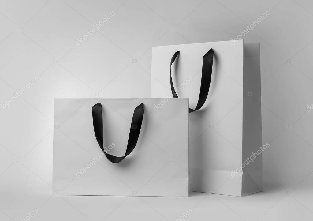 Paper shopping bags with ribbon handles on white background. Mockup for design